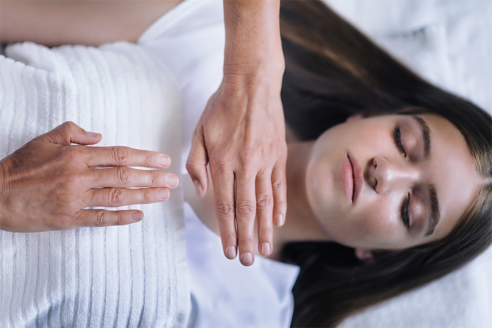 Reiki: Behandlung mit zwei Händen über Hals und Brustbereich bei Frau in Rückenlage