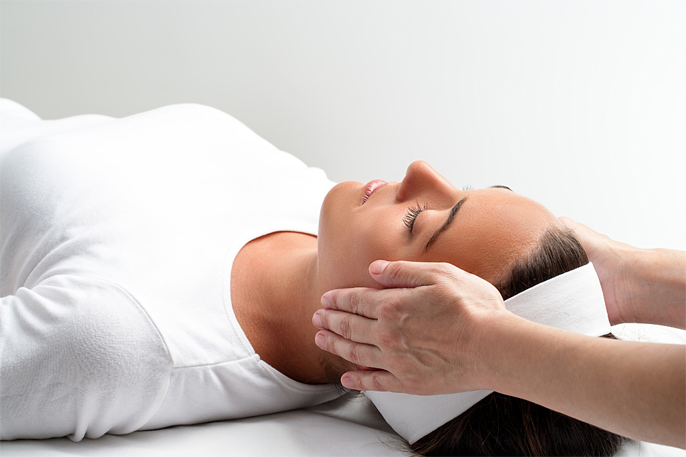 Reiki: Behandlung über den Ohren bei Frau in Rückenlage