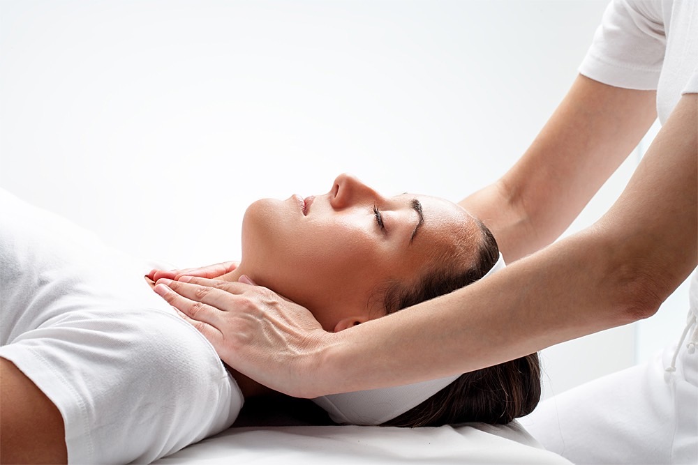 Reiki: Behandlung mit zwei Händen über Hals und Brustbereich bei Frau in Rückenlage