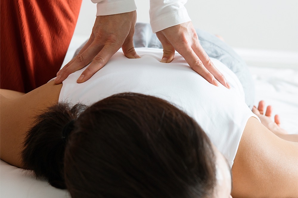 Shiatsu: Behandlung mit der Daumentechnik am Rücken bei Frau in Bauchlage